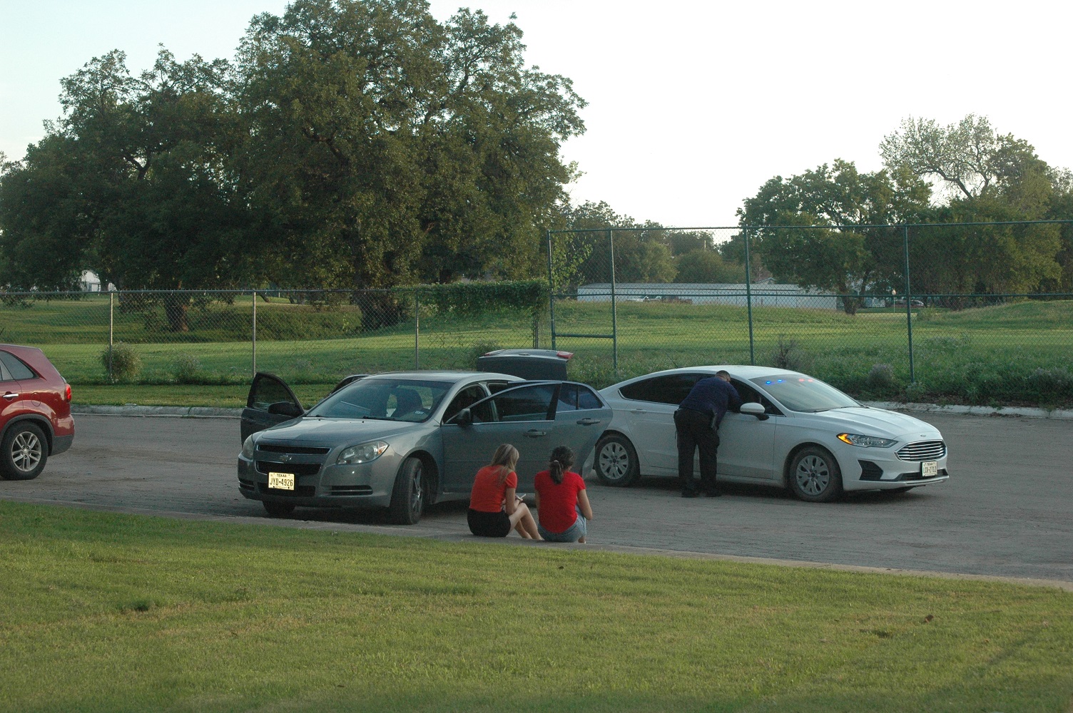 Two females sit nearby a vehicle as it is being searched by police