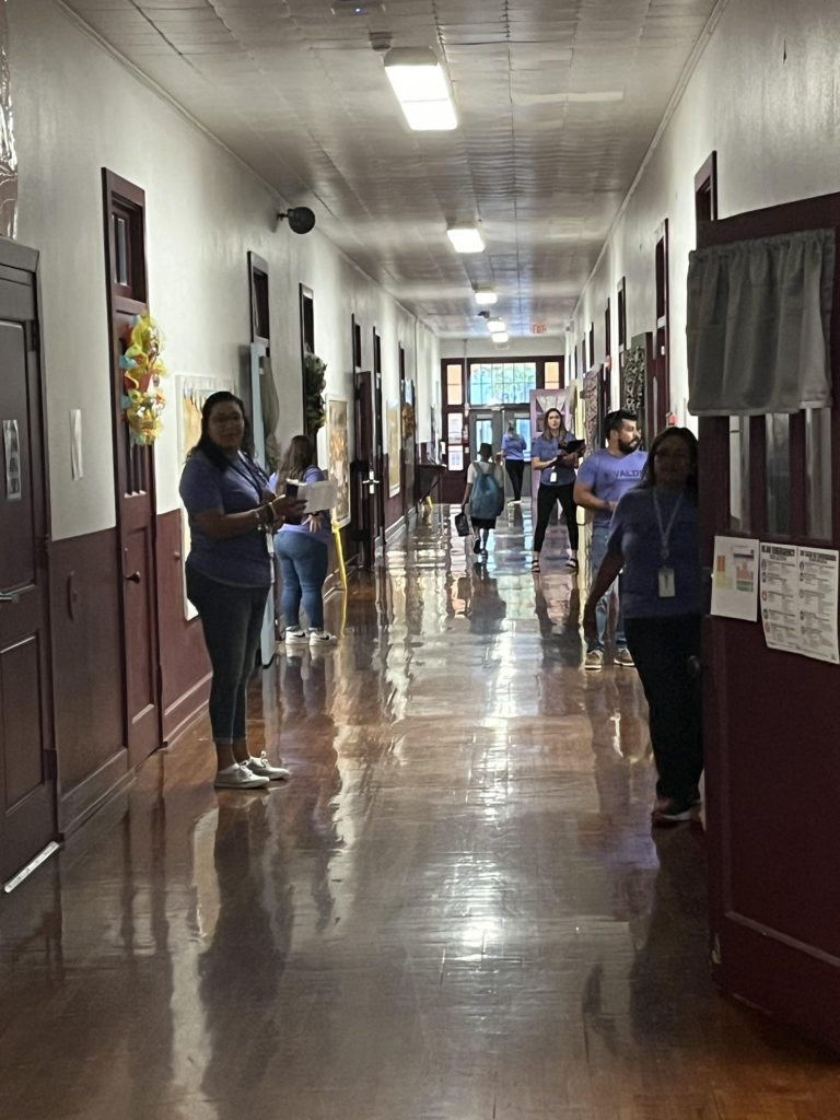 Teachers line up in the hallway by the doors of their respective classrooms